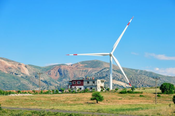Wind turbine and house on a hill under a blue sky. Element of a wind power station. Alternative energy concept. Turkey